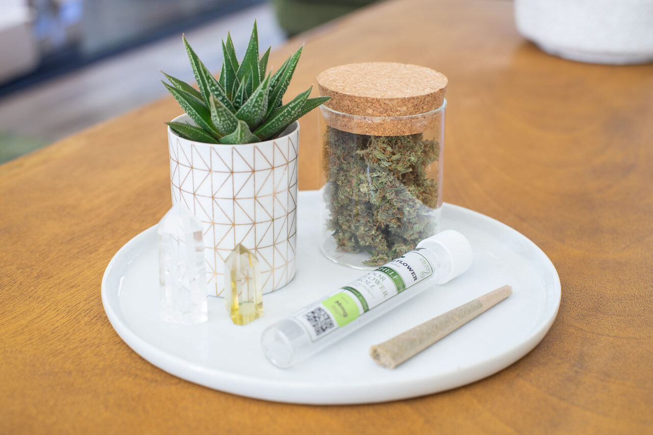 A Top Shelf Indoor PreRoll on a plate with the labeled tube, a plant, some crystals and a jar of premo hemp flower.